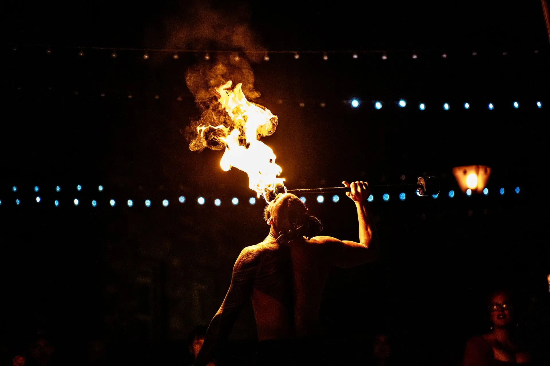 A man is blowing fire from his mouth in a dark room.
