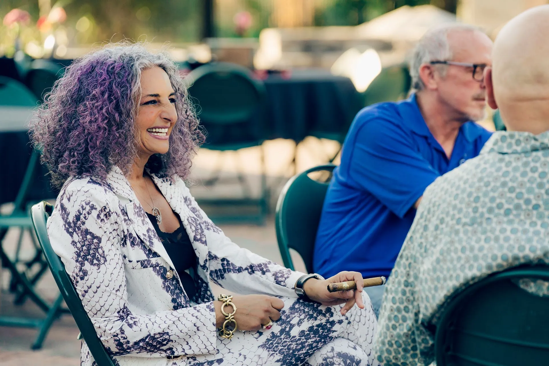A woman with purple hair is sitting in a chair talking to two men.