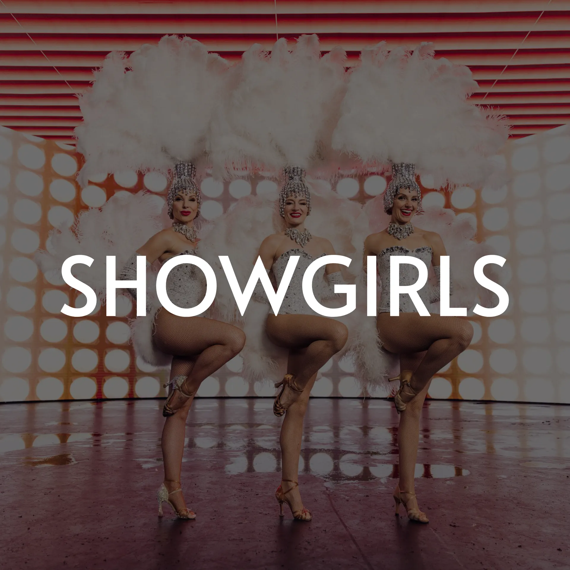 Three showgirls in elaborate headdresses and costumes, posing on a stage with a dotted backdrop.