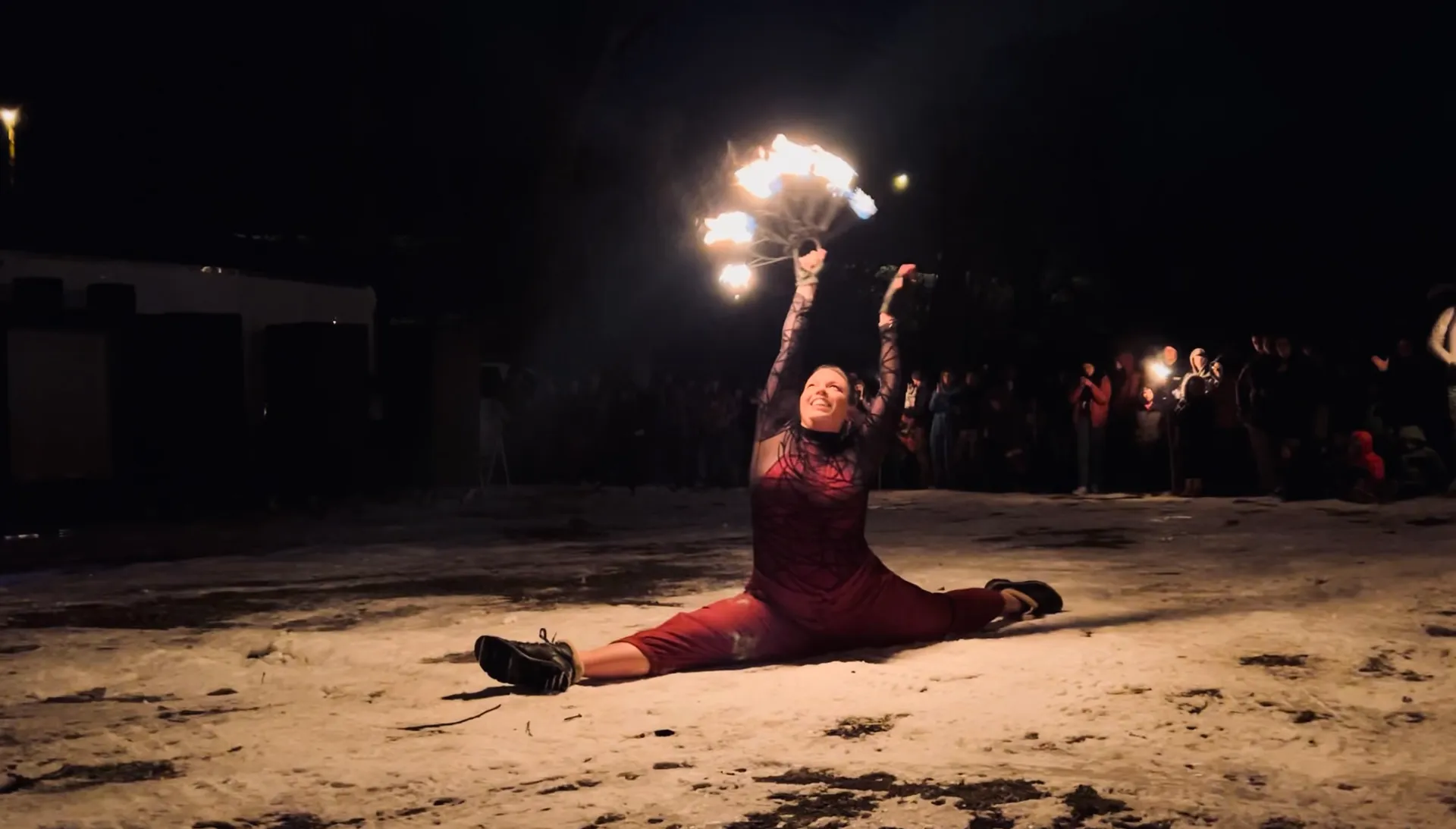 A woman is doing a split while holding a fan of fire.