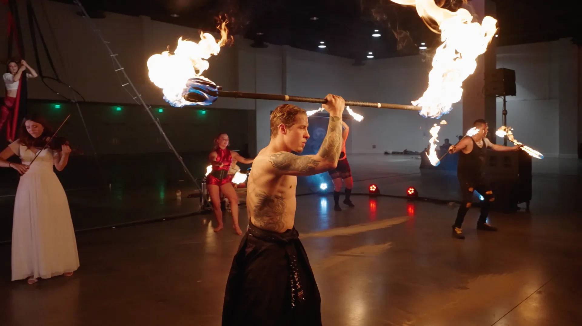 A group of people are performing a fire show in a large room.