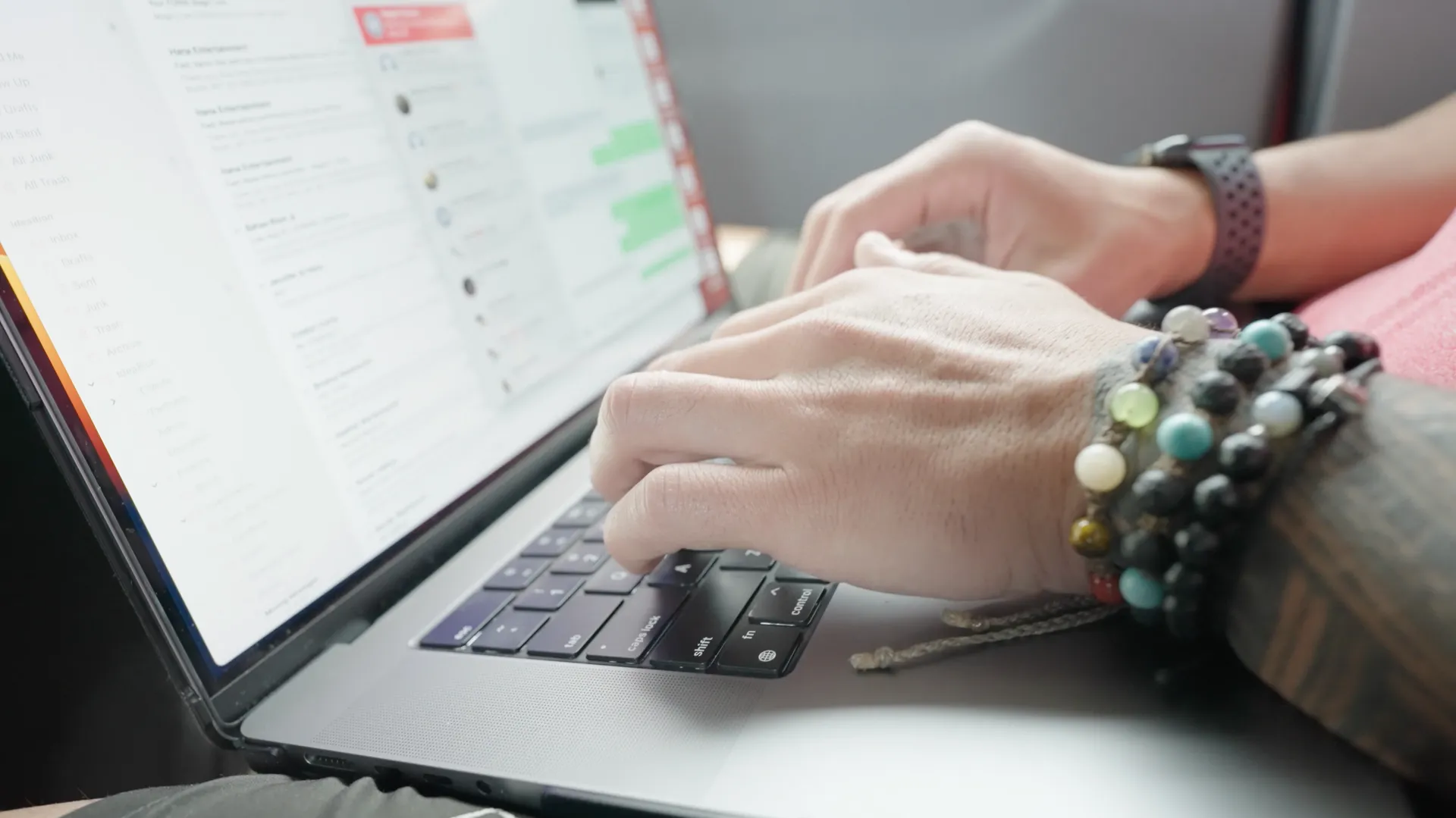 A person wearing bracelets is typing on a laptop computer.