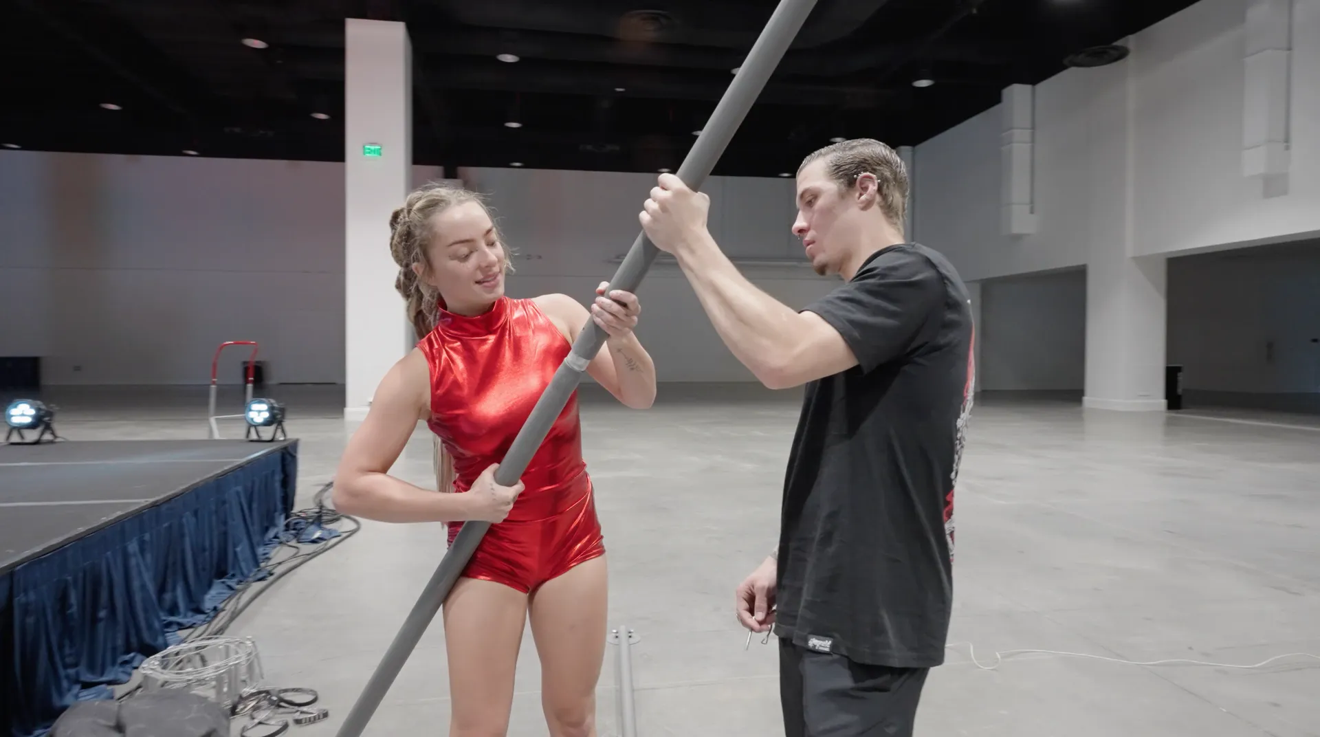 A man and a woman are holding a pole in an empty room.