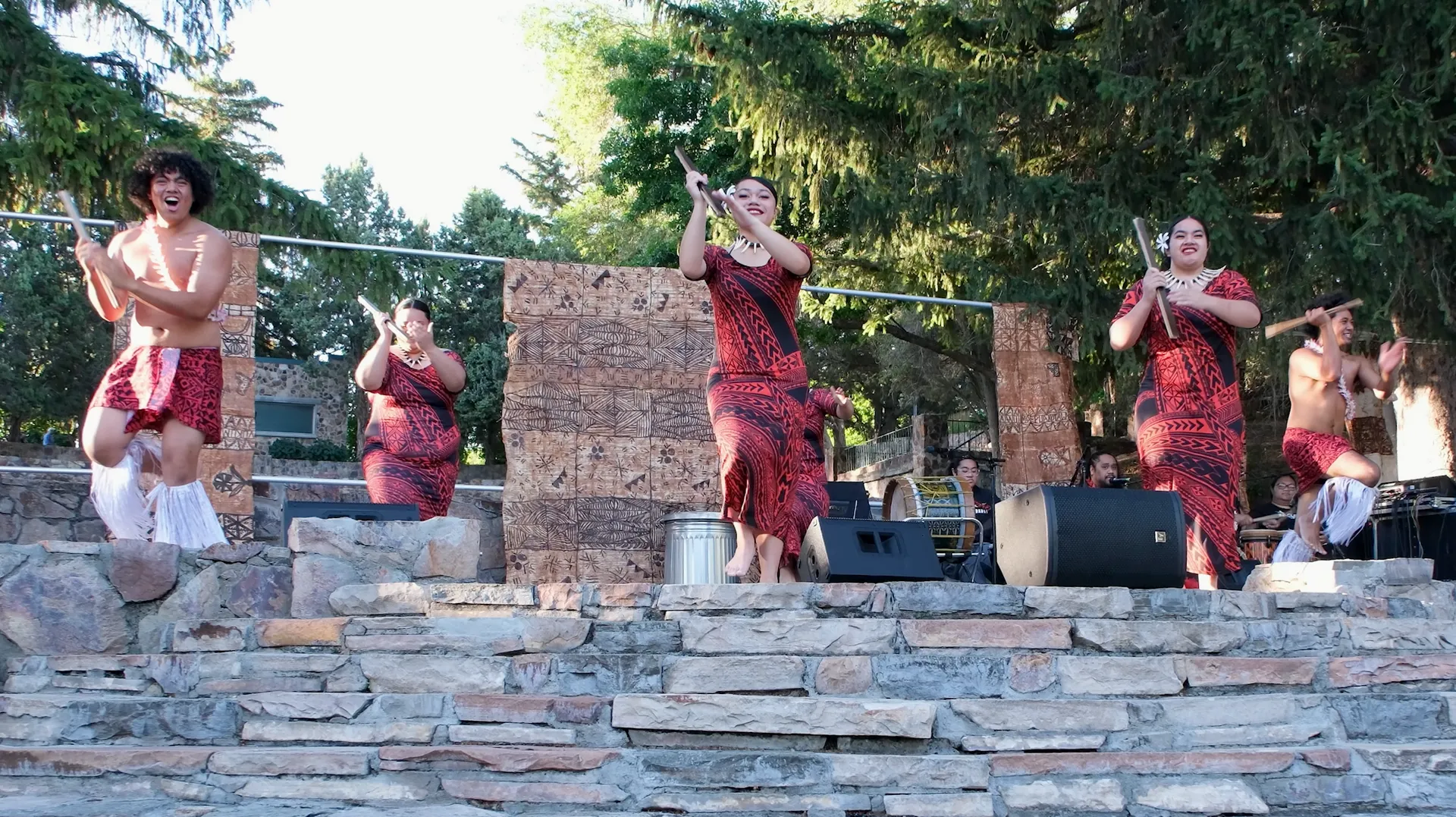 A group of people are performing on a stage in front of a stone wall.