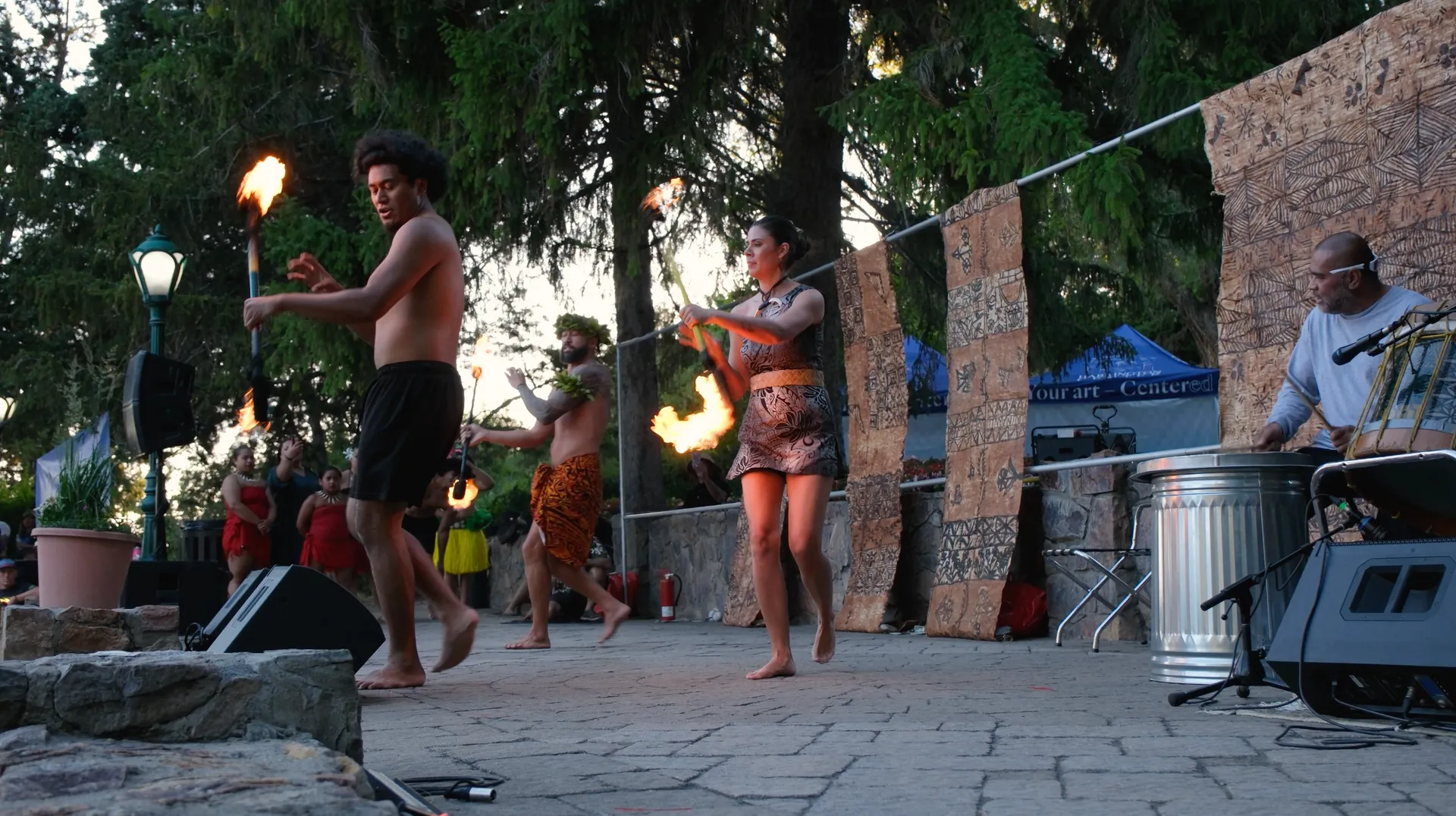 A group of people are dancing on a stage with fire torches.
