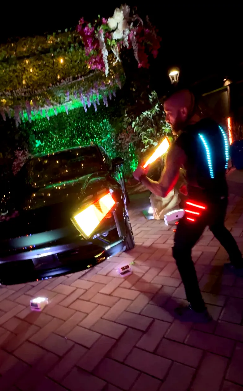 A man is holding a light up stick in front of a car.