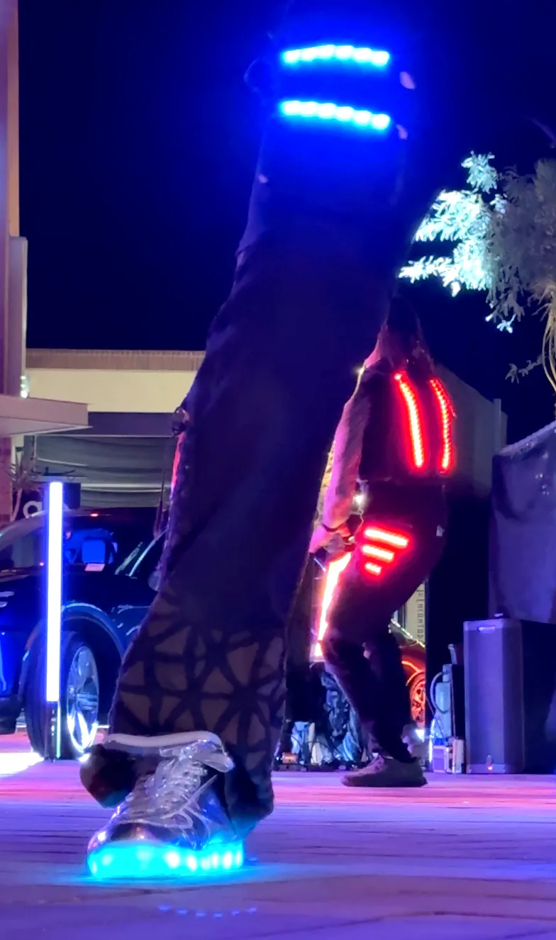 A person wearing glow in the dark roller skates is standing on a street at night.