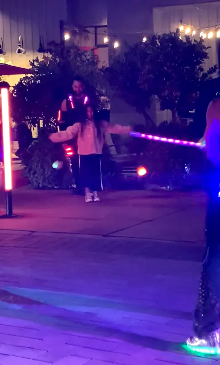 A person is holding a light saber in front of a little girl.