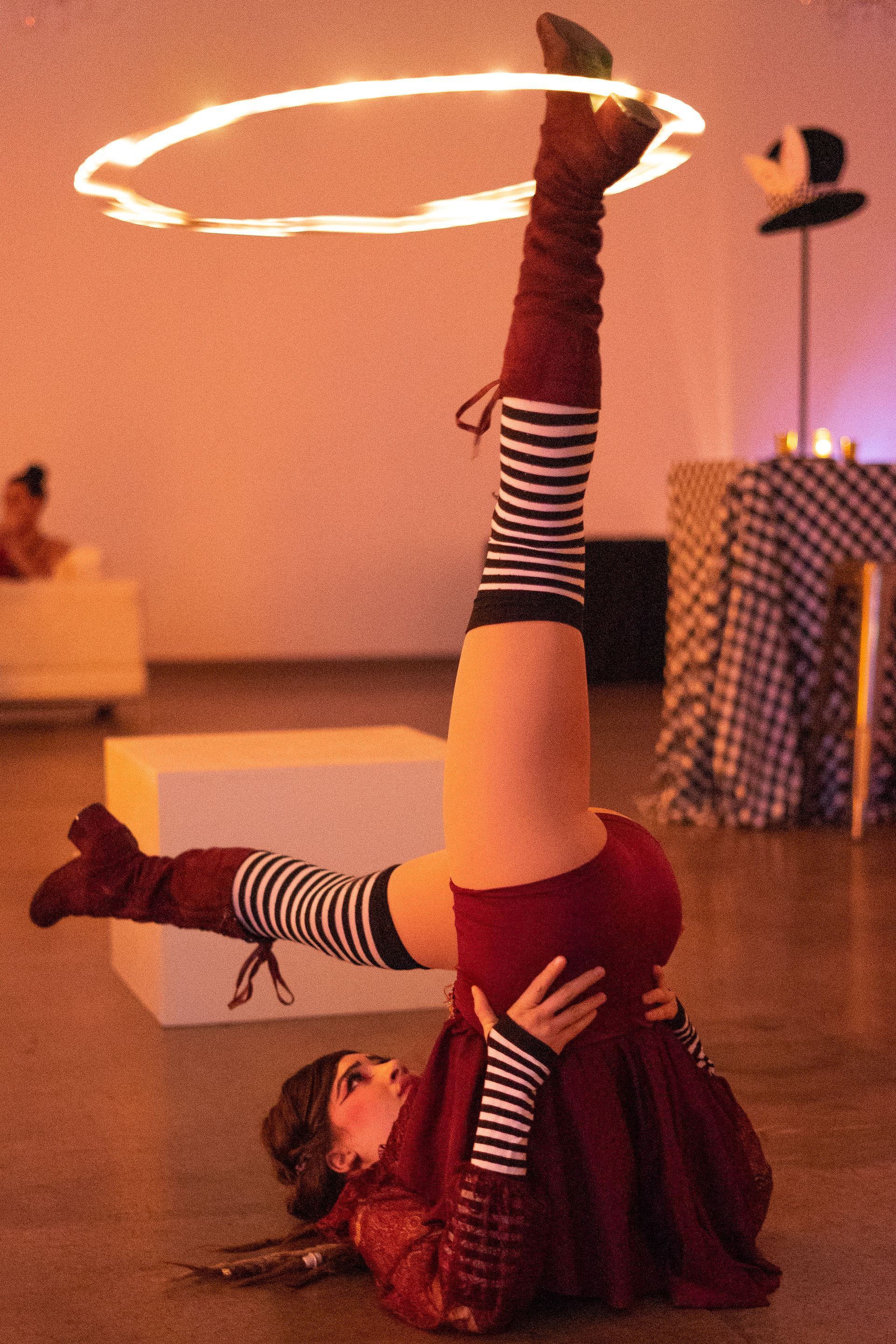 A woman is doing a handstand with a fire hoop around her waist.