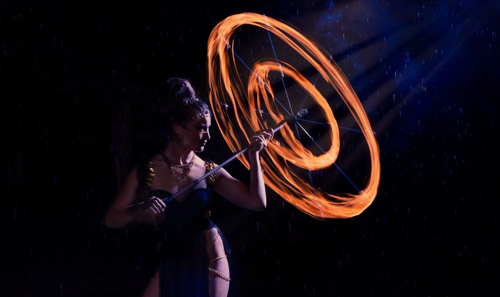 A woman in a black dress is spinning a fire poi in the dark.