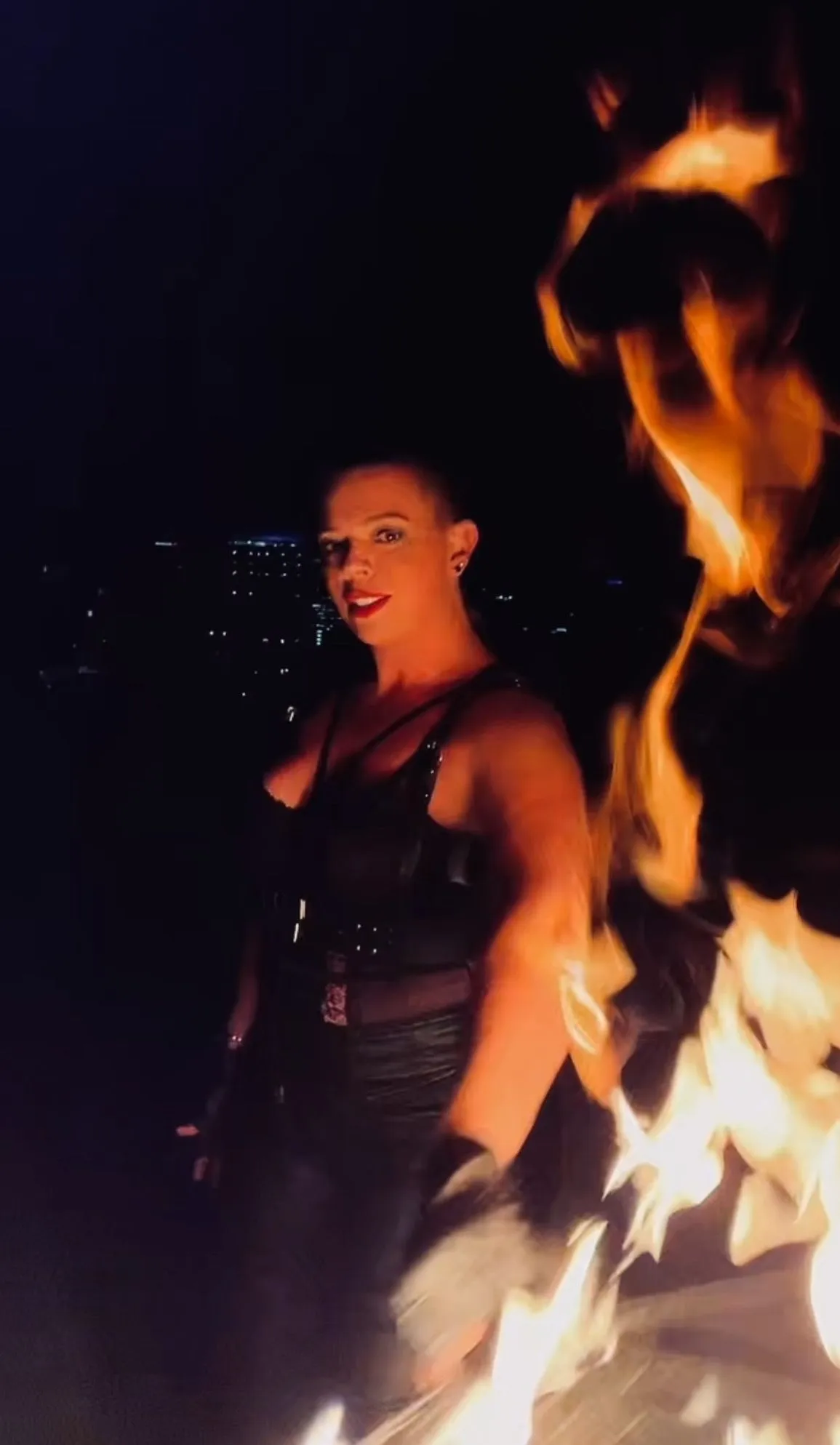 A woman is standing in front of a large fireball in the dark.