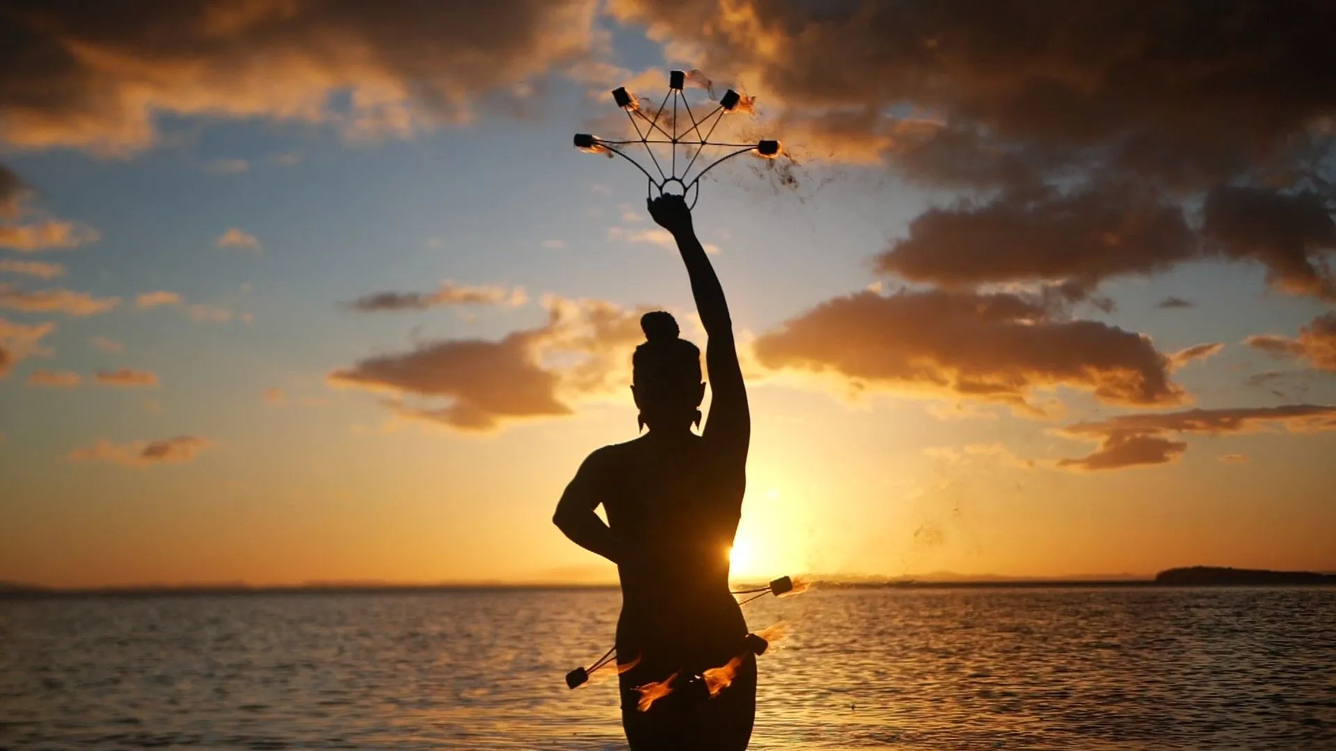 A woman is standing in the water holding a flower in her hand at sunset.