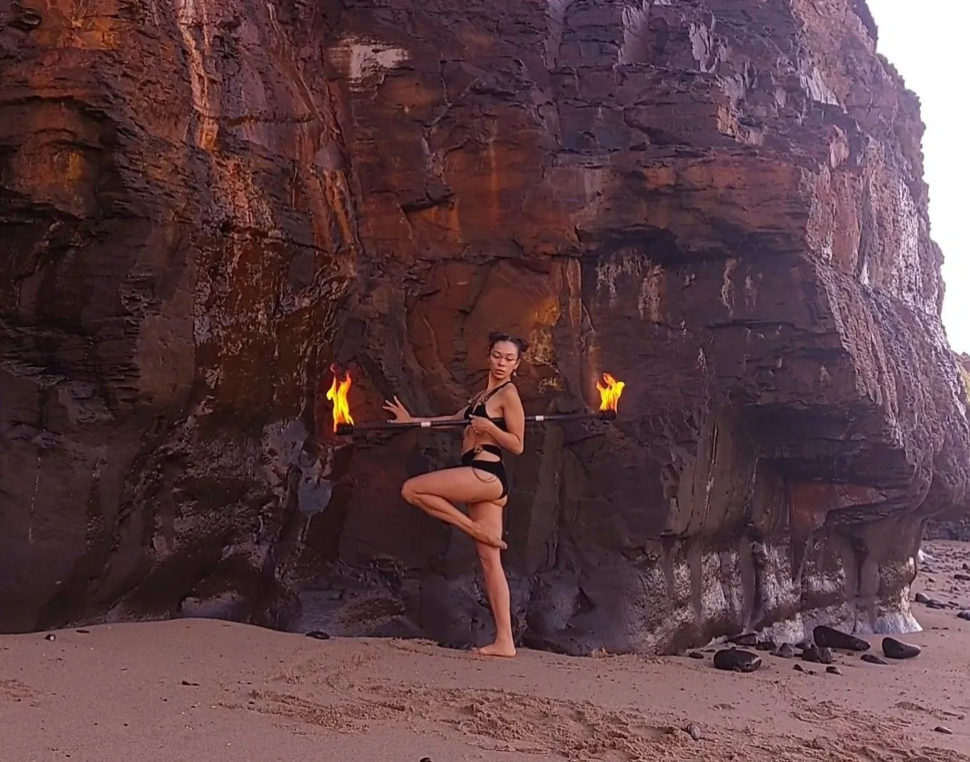 A woman in a bikini is standing on a beach holding two fire sticks.