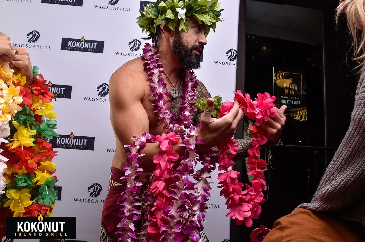 A shirtless man is wearing a lei and holding flowers.
