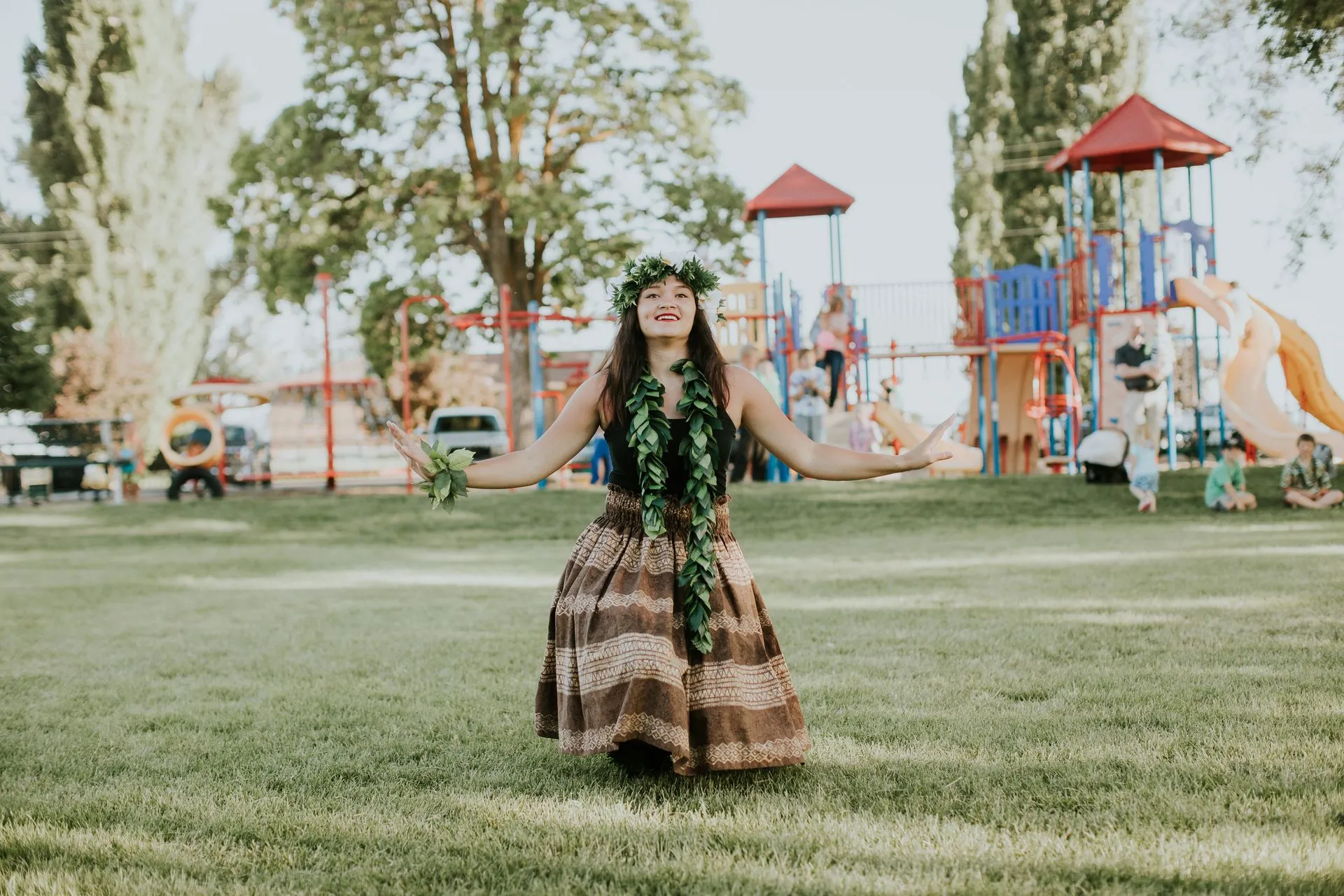 A woman in a hula dress is dancing in a park.