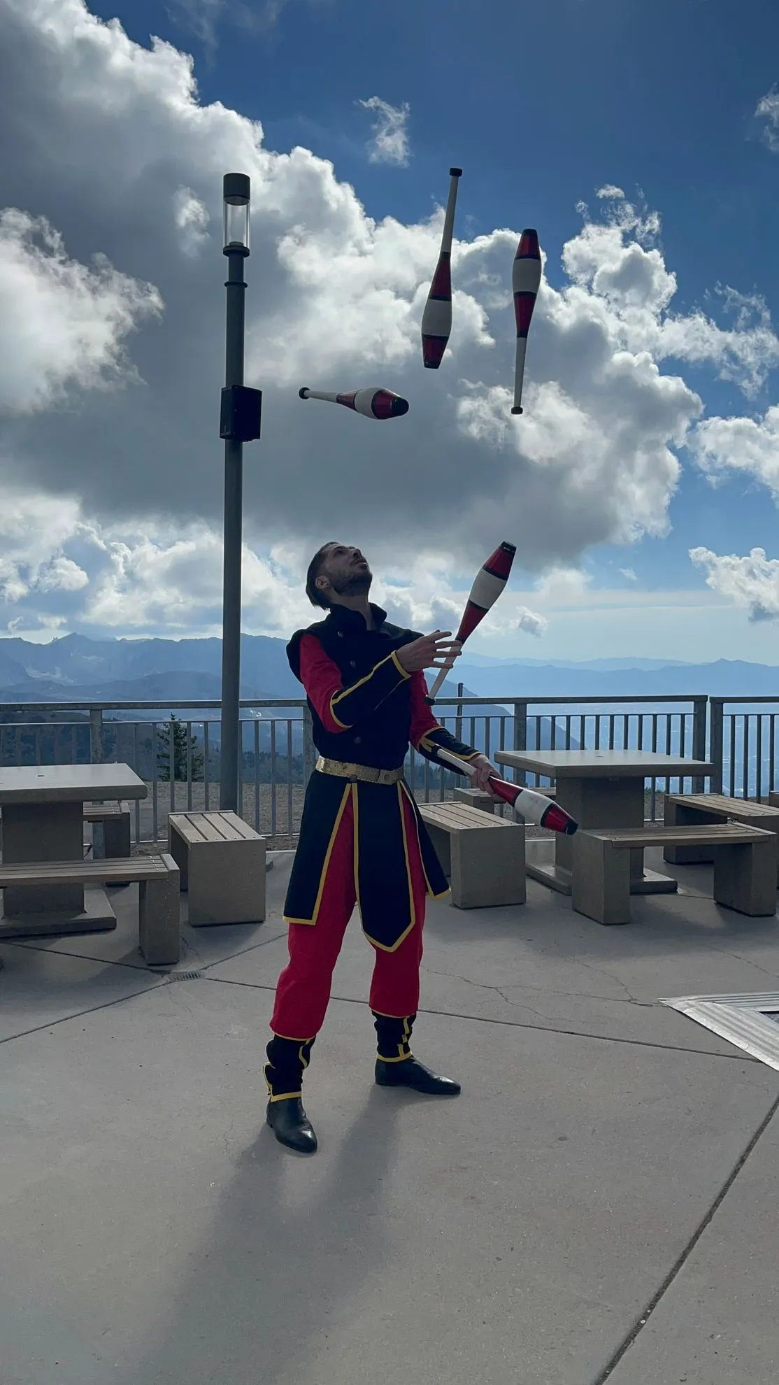A man in a costume is juggling clubs on a balcony.