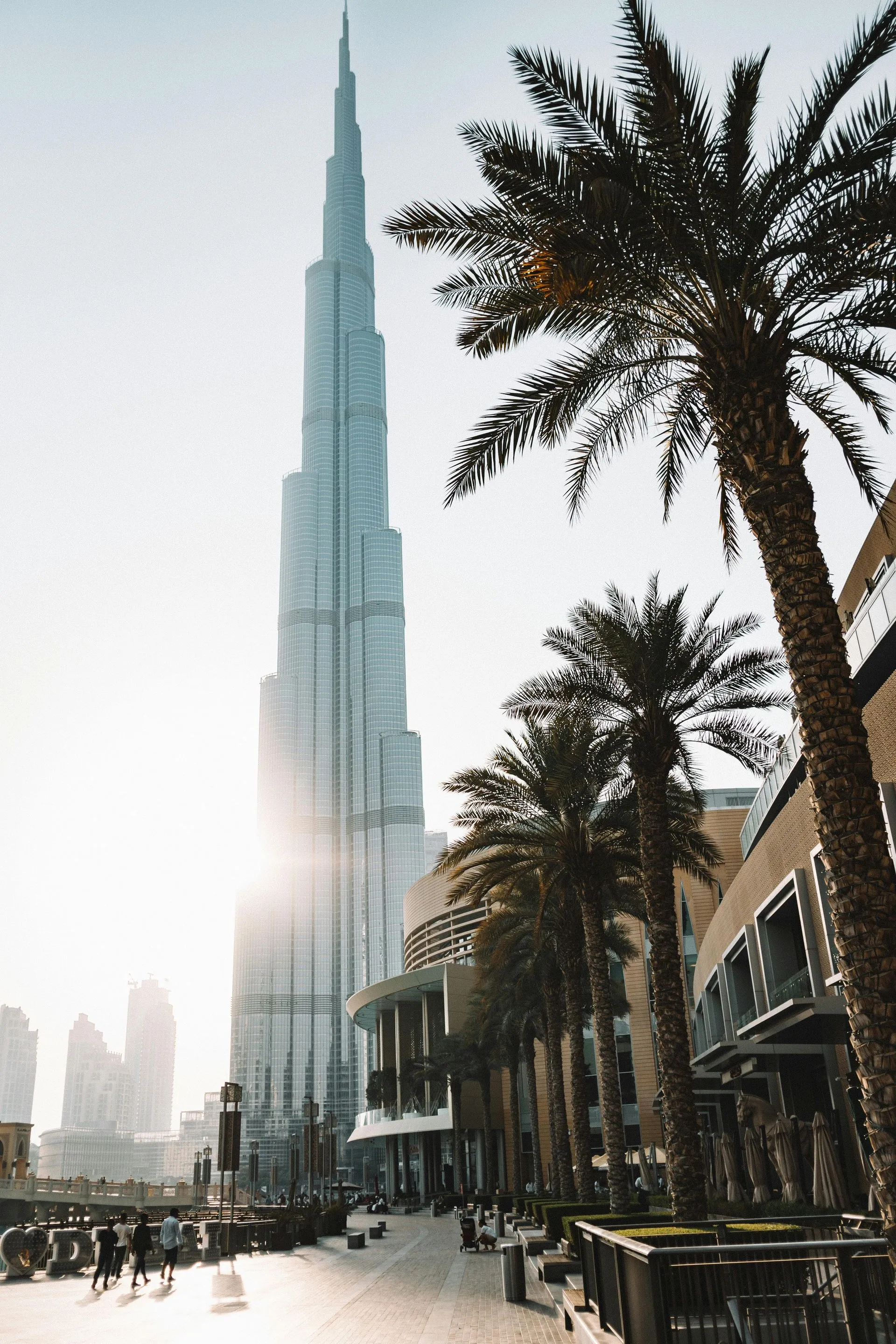 Burj Khalifa skyscraper in Dubai, with palm trees and a sunny sky.