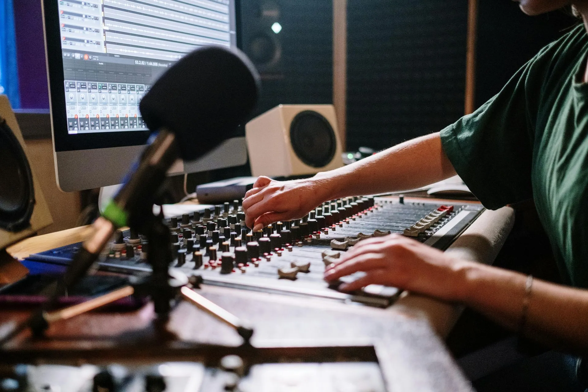 Person at a mixing console in a recording studio, adjusting knobs near microphone.
