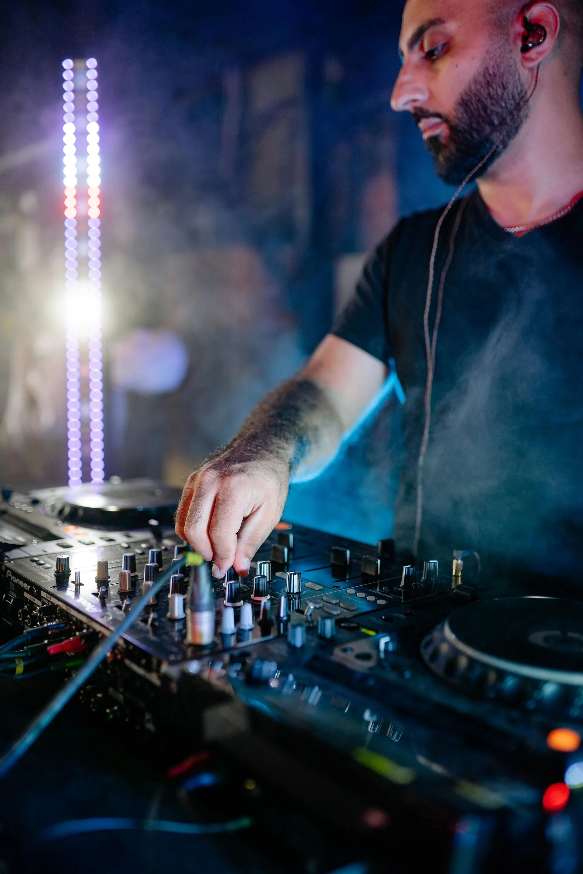 DJ mixing music at a club with smoke and a light display.
