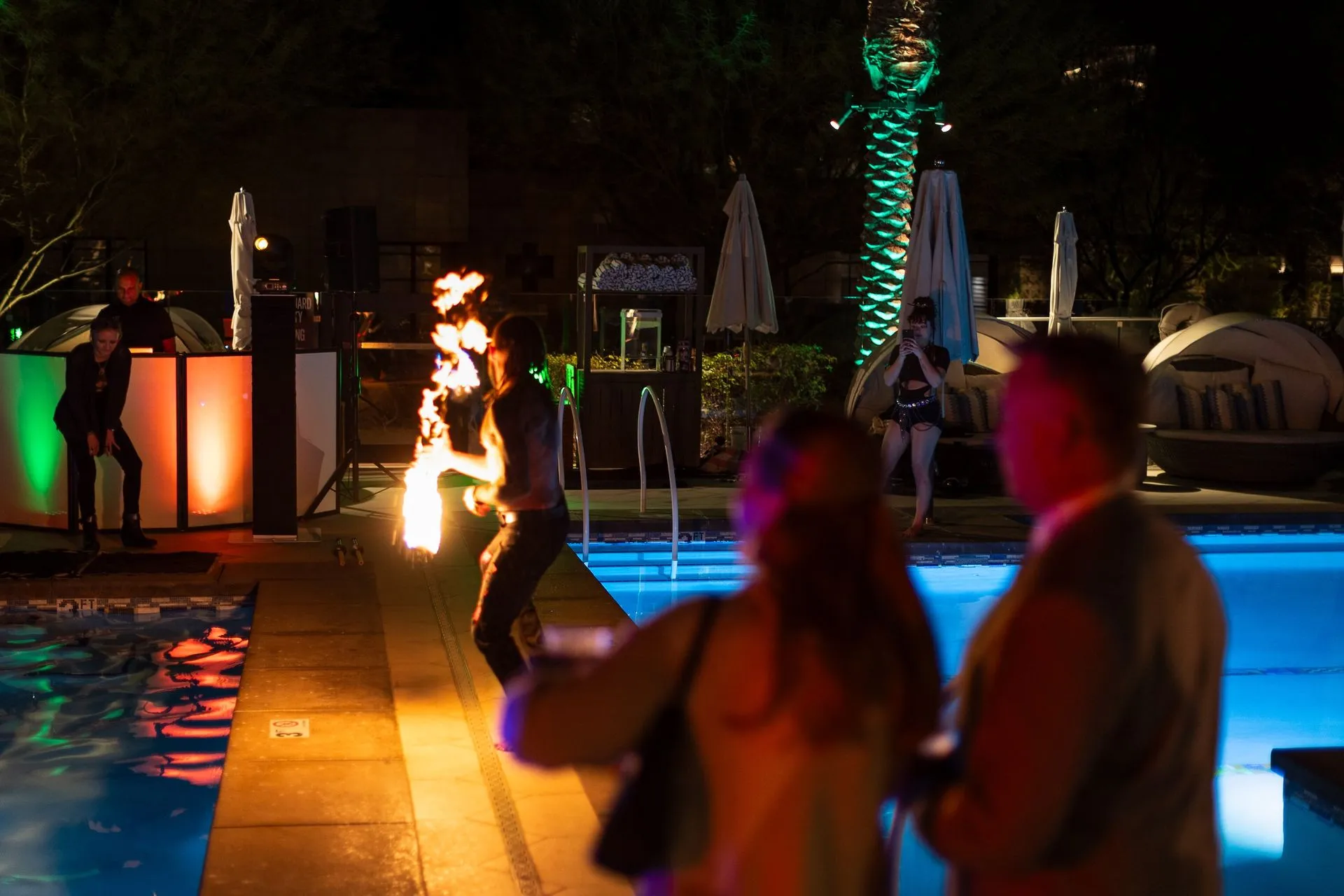 Fire performer on pool deck at night with illuminated structures and lit palms in background